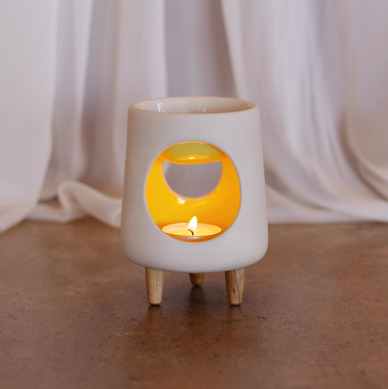 Ceramic wax warmer essential oil warmer by Arya Tara Candles. White outside yellow inside colored. Ceramic handmade tealight wax warmer with wooden legs.