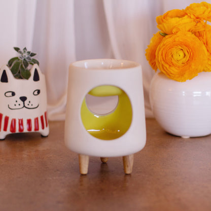 Ceramic wax warmer essential oil warmer by Arya Tara Candles. White outside yellow inside colored. Ceramic handmade tealight wax warmer with wooden legs.
