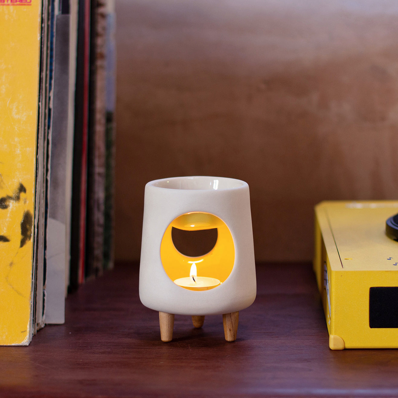Ceramic wax warmer essential oil warmer by Arya Tara Candles. White outside yellow inside colored. Ceramic handmade tealight wax warmer with wooden legs.